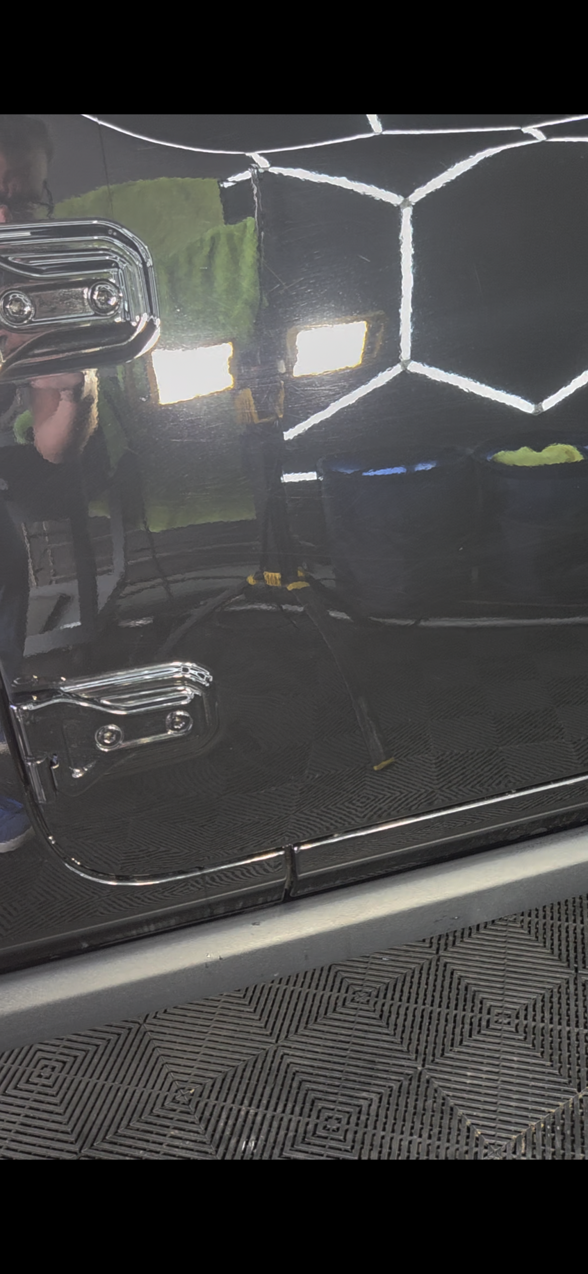 Door of a black Jeep Wrangler Rubicon before paint correction, with swirl marks and light scratches around the reflection of a work light